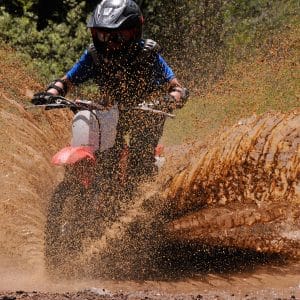 Kid on dirtbike splashes puddle during private lesson.