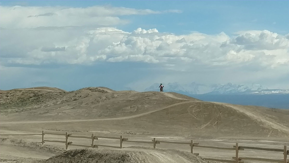 Picture of kid dirtbiking on the adobe or silt mounds with the mountains in the background