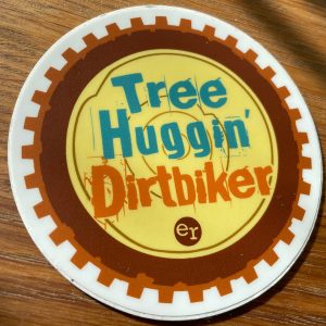 Round sticker that says "tree huggin' dirtbiker"